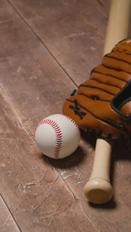 Vertical-Video-Close-Up-Studio-Baseball-Still-Life-With-Wooden-Bat-And-Ball-In-Catchers-Mitt-On-Wooden-Floor